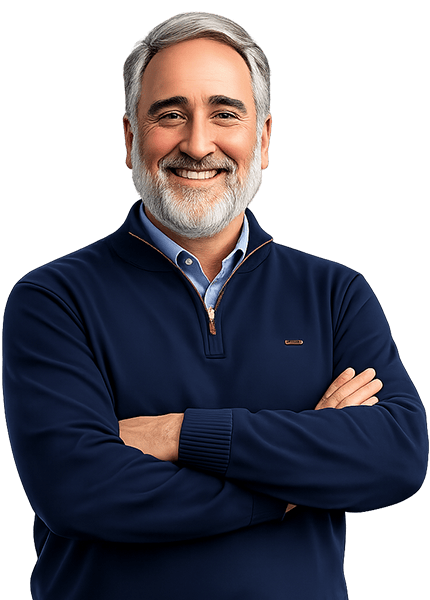 Smiling Ed Bejarana with short grey hair and a well-groomed grey beard, wearing a navy blue quarter-zip sweater over a light blue button-down shirt, standing with arms crossed against a white background.